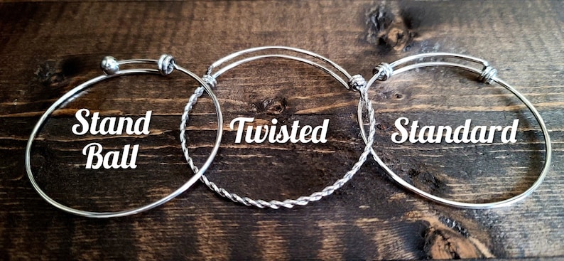 May include: Three silver expandable bracelets with different styles: a standard bracelet, a twisted bracelet, and a stand ball bracelet. The bracelets are on a wooden background.
