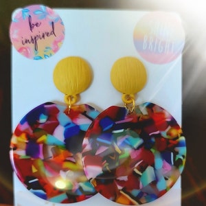 May include: A pair of colorful, round earrings with a yellow top. The earrings have a multi-colored, confetti-like pattern.