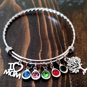 May include: A silver expandable bangle bracelet with charms. The charms include a heart with "I love Mom" written on it, a small tree, and five colorful teardrop-shaped crystals.