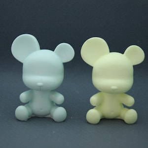 May include: Two small, unpainted, ceramic teddy bear figurines. One is light blue and the other is light yellow.