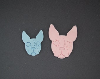 May include: Two dog-shaped cookie cutters, one light blue and one pink, with heart-shaped eyes.