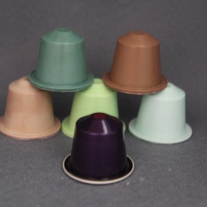Può includere: Sei capsule di caffè monodose in vari colori, tra cui verde, marrone, verde chiaro, blu chiaro e viola. Le capsule sono impilate l'una sull'altra.