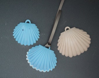Op de afbeelding: Drie decoratieve schelpen, twee blauwe en één beige, op een donkergrijs oppervlak. De blauwe schelpen hebben een witte rand.