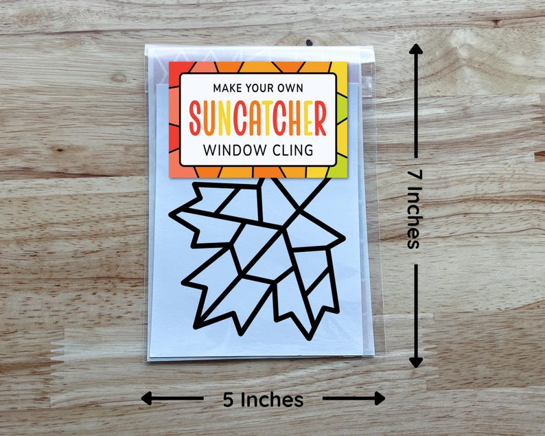 Op de afbeelding: Een Make Your Own Suncatcher raamsticker-set met een zwarte omtrek van een esdoornblad op een witte achtergrond. Het verpakkingslabel heeft kleurrijke geometrische randen en meet 17,78 cm hoog bij 12,7 cm breed.