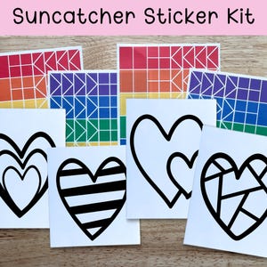 May include: A Suncatcher Sticker Kit featuring various designs. The kit includes stickers with geometric rainbow patterns and black heart designs. The text "Suncatcher Sticker Kit" is at the top of the image. The stickers are on a wooden surface.