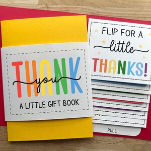 May include: A colorful "Thank You" gift book with a red envelope. The book has a yellow cover and features the text "Thank You" in rainbow colors. The inside pages say "Flip for a little Thanks!"