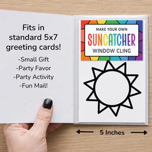 Op de afbeelding: Een suncatcher raamsticker set van 12,7 bij 17,8 cm. De verpakking heeft een regenboogrand en de tekst 'MAKE YOUR OWN SUNCATCHER WINDOW CLING' boven een zwarte zonomtrek. De tekst op de kaart luidt 'Fits in standard 5x7 greeting cards!'
