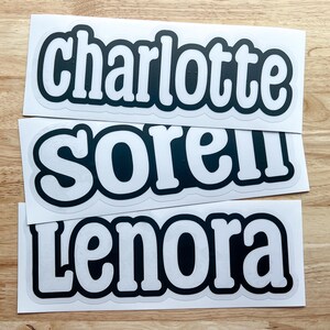 K&ouml;nnte beinhalten: Drei wei&szlig;e Aufkleber mit schwarzem Text. Der obere Aufkleber sagt "charlotte", der mittlere Aufkleber sagt "sorel" und der untere Aufkleber sagt "lenora".