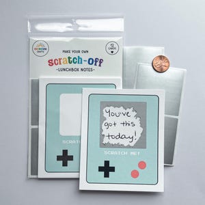 May include: A package of "Make Your Own Scratch-Off Lunchbox Notes" cards. The cards are designed like a retro handheld game console in light blue, with a gray scratch-off area and the text "You've got this today!"