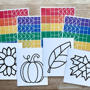Op de afbeelding: Een set knutselbenodigdheden bestaande uit vier rechthoekige vellen met regenboogkleurige geometrische rasterpatronen en vier witte vierkante kaarten met zwarte lijntekeningen van een zonnebloem, een pompoen, een blad en een esdoornblad.