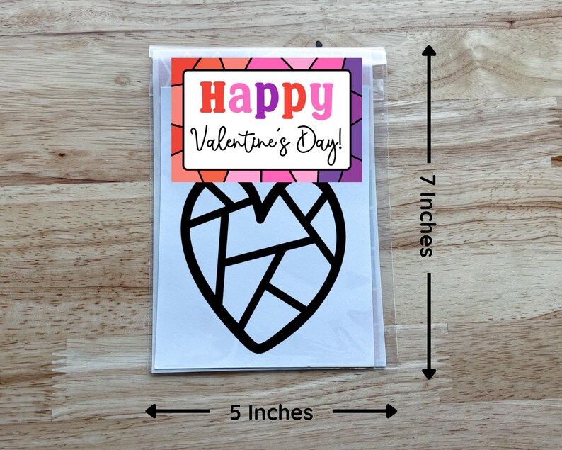 May include: A Valentine's Day card in a clear plastic sleeve. The card features a black geometric heart design and the words "Happy Valentine's Day!" in a colorful frame. The card measures 5 inches wide and 7 inches tall.