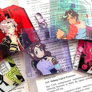 Op de afbeelding: Een verzameling van zes kleurrijke plastic badges met anime-achtige personages. De badges zijn versierd met tekst, waaronder "No. 2 Snake", "No. 5 June", "No. 4 Over" en "LPO C".