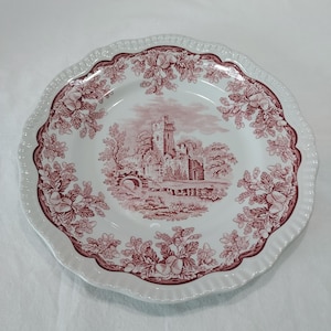 May include: A white ceramic dinner plate with a scalloped edge and a maroon transferware pattern. The center features a detailed illustration of a stone castle and bridge, while the rim is decorated with a repeating motif of oak leaves and acorns.