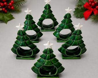 Könnte beinhalten: Ein Set aus sechs Serviettenringen aus Keramik in Form von Weihnachtsbäumen. Jeder Baum ist mit einer tiefgrünen Glasur mit glänzendem Finish überzogen und an der Spitze mit einem kleinen, weißen, fünfzackigen Stern versehen.