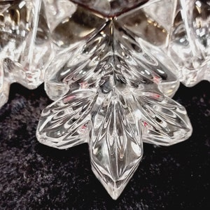 K&ouml;nnte beinhalten: Ein klarer gl&auml;serner Schneeflocken-Anh&auml;nger mit filigranen Details. Die Schneeflocke hat eine sechszackige Sternform mit einem Mittelpunkt und sechs Armen.
