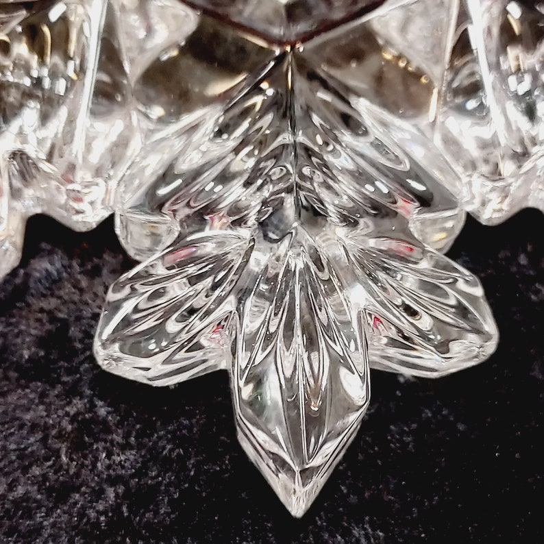 K&ouml;nnte beinhalten: Ein klarer gl&auml;serner Schneeflocken-Anh&auml;nger mit filigranen Details. Die Schneeflocke hat eine sechszackige Sternform mit einem Mittelpunkt und sechs Armen.