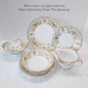 May include: A collection of white porcelain dishware with gold floral and scrollwork designs. The set includes plates, bowls, a gravy boat, and a covered serving dish. The text on the image reads "Meito China Lee Gold Collection Make Selection(s) From This Grouping."