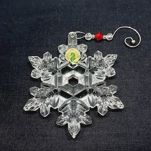 Stunning ornament with decorative hanger is in excellent condition and in original box which shows minimal wear. Clear crystal with hand-cut texturing on a snowflake design. It measures approximately 4-1/2" x 4" x 1/2", and with the hanger in place, the ornament extends to about 7-1/2" long. Made in Slovenia. Waterford 2014 Annual Christmas Ornament