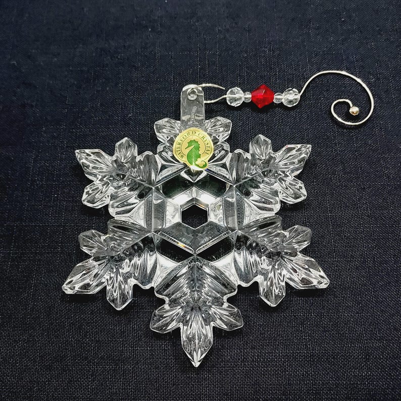 Stunning ornament with decorative hanger is in excellent condition and in original box which shows minimal wear. Clear crystal with hand-cut texturing on a snowflake design. It measures approximately 4-1/2" x 4" x 1/2", and with the hanger in place, the ornament extends to about 7-1/2" long. Made in Slovenia. Waterford 2014 Annual Christmas Ornament