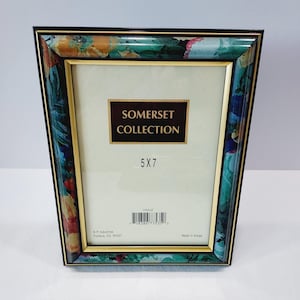 May include: A decorative photo frame from the Somerset Collection. The frame has a floral pattern in shades of blue, green, and yellow. The frame is 5x7 inches with a gold-colored inner border and black outer border.