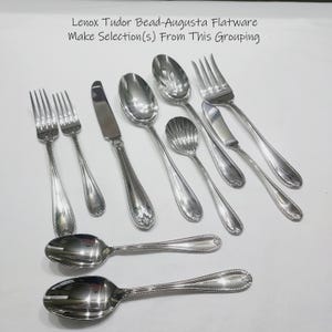May include: A collection of Lenox Tudor Bead-Augusta flatware, including forks, spoons, knives, and serving spoons. The silverware has a shiny, silver finish with a beaded edge design. The text in the image reads: Lenox Tudor Bead-Augusta Flatware Make Selection(s) From This Grouping.