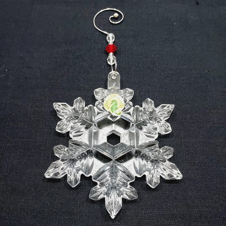 Stunning ornament with decorative hanger is in excellent condition and in original box which shows minimal wear. Clear crystal with hand-cut texturing on a snowflake design. It measures approximately 4-1/2" x 4" x 1/2", and with the hanger in place, the ornament extends to about 7-1/2" long. Made in Slovenia. Waterford 2014 Annual Christmas Ornament