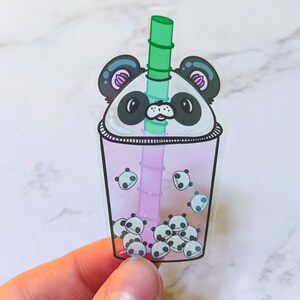 Op de afbeelding: Een transparante sticker van plastic met een roze en paarse boba-thee met een panda-gezicht bovenop en kleinere panda-gezichten in de drank. De boba-thee heeft een groene rietje.