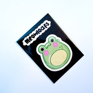 May include: A black and white sticker with the text "MEOWOOAFS" and a green cartoon frog with pink cheeks.