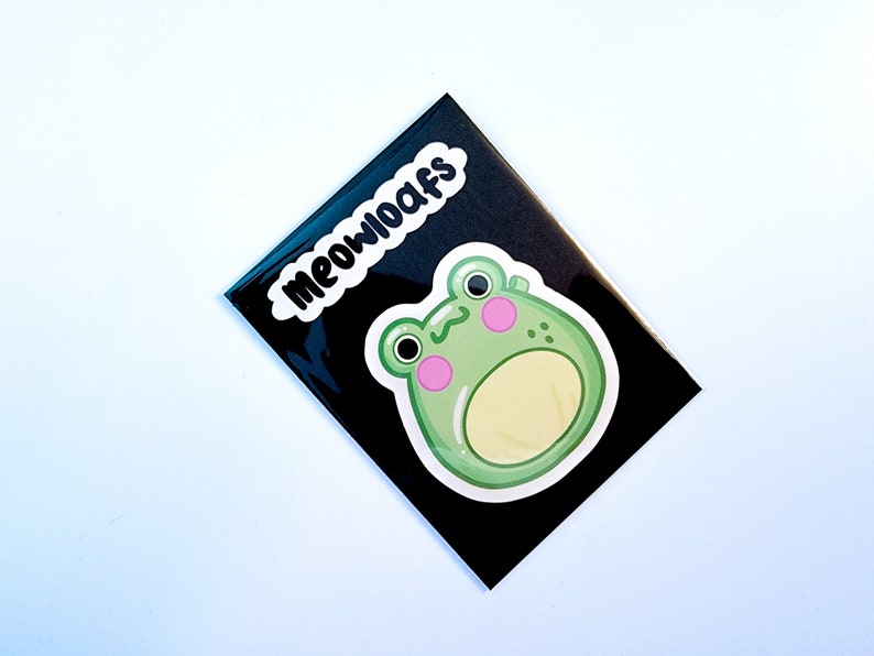 May include: A black and white sticker with the text "MEOWOOAFS" and a green cartoon frog with pink cheeks.