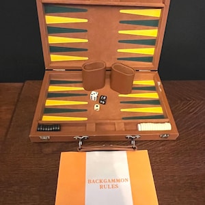 May include: A brown leather backgammon game set with a green and yellow playing board, dice, and checkers. The set is open and the board is visible. The set also includes a small booklet with the text "Backgammon Rules".