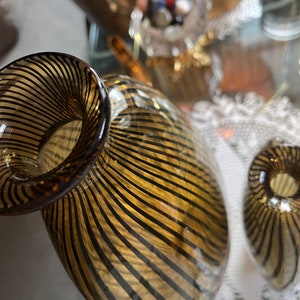 Op de afbeelding: Twee glazen vazen met een gestreept patroon in tinten bruin en goud. De vazen zijn rond en hebben een brede opening aan de bovenkant.