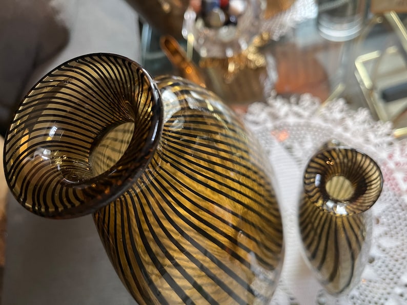 Op de afbeelding: Twee glazen vazen met een gestreept patroon in tinten bruin en goud. De vazen zijn rond en hebben een brede opening aan de bovenkant.