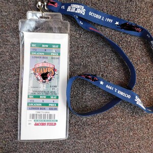 May include: A blue lanyard with the text "TORONTO BLUE JAYS OCTOBER 3, 1999" and a white ticket with the text "JACOBS FIELD" and "CHAMPS".