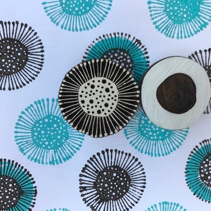 May include: Three wooden printing blocks with circular designs. The blocks are black, white and brown. The designs feature a circle with a smaller circle inside, surrounded by radiating lines.