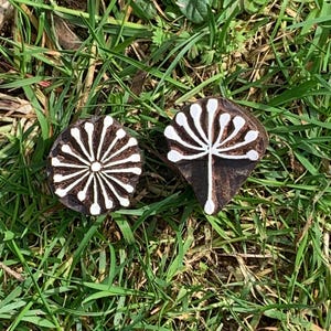 May include: Two dark brown wooden printing blocks with white carved designs. The left block features a circular pattern with radiating lines, while the right block displays a fan-shaped floral motif with a central stem and branching petals.