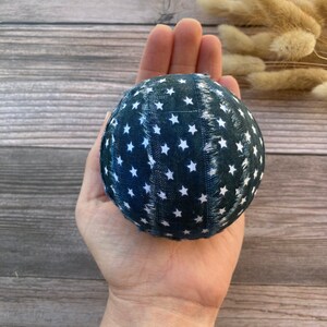 Puede incluir: Una bola de tela azul con estrellas blancas, sostenida en una mano. La bola est&aacute; hecha de tela con un borde deshilachado.