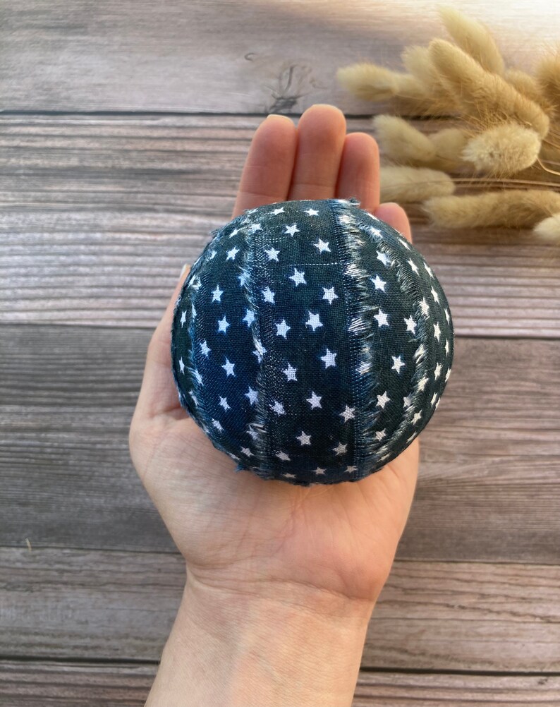 Puede incluir: Una bola de tela azul con estrellas blancas, sostenida en una mano. La bola est&aacute; hecha de tela con un borde deshilachado.