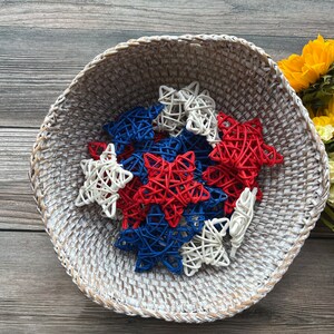 May include: A white wicker basket filled with red, white, and blue star-shaped decorations. The stars are made of woven material and are a festive decoration for a patriotic holiday.