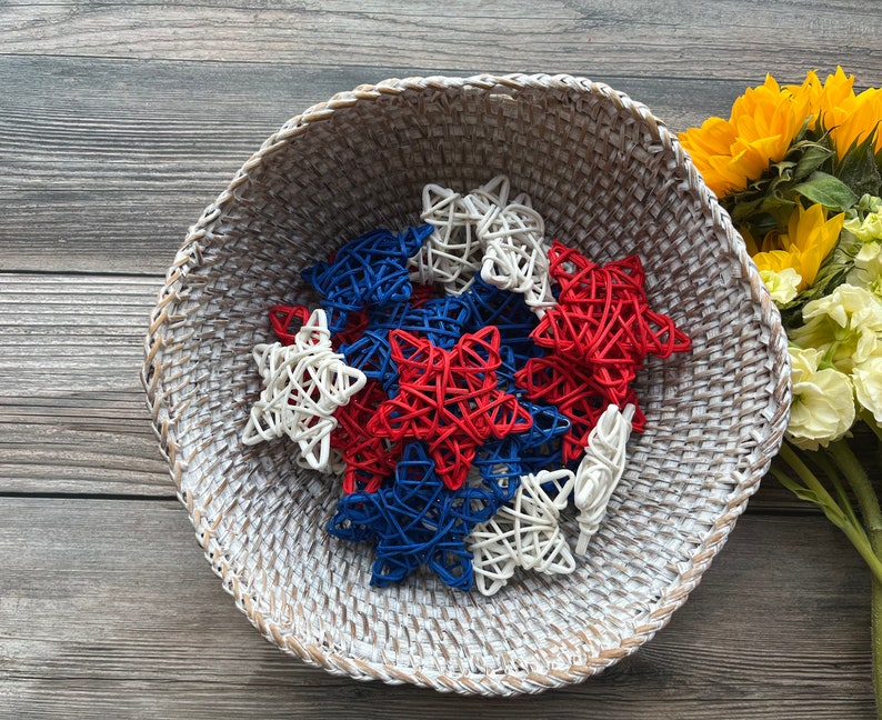 May include: A white wicker basket filled with red, white, and blue star-shaped decorations. The stars are made of woven material and are a festive decoration for a patriotic holiday.