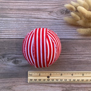 Puede incluir: Una bola de adorno de tela a rayas rojas y blancas. La bola tiene un di&aacute;metro de aproximadamente 5 cm.