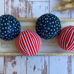 Puede incluir: Cuatro bolas decorativas en una bandeja de madera. Dos bolas son azules con estrellas blancas y dos bolas son rojas con rayas blancas.