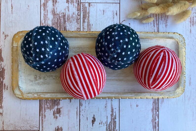 Puede incluir: Cuatro bolas decorativas en una bandeja de madera. Dos bolas son azules con estrellas blancas y dos bolas son rojas con rayas blancas.
