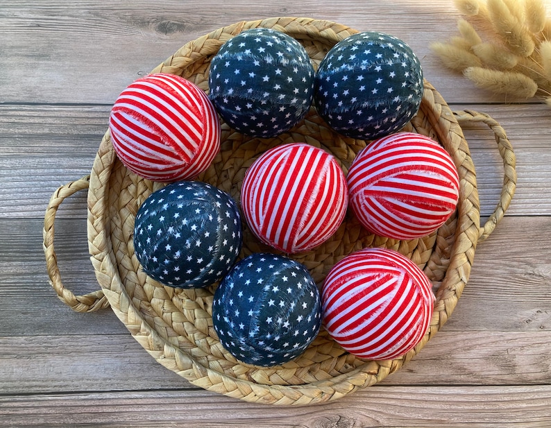 Puede incluir: Una cesta de mimbre llena de ocho bolas de tela. Las bolas est&aacute;n decoradas con rayas rojas y blancas y estrellas azules, que se asemejan a la bandera espa&ntilde;ola.