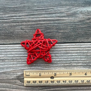 May include: A red woven star ornament, approximately 2 inches in diameter, on a woodgrain background.