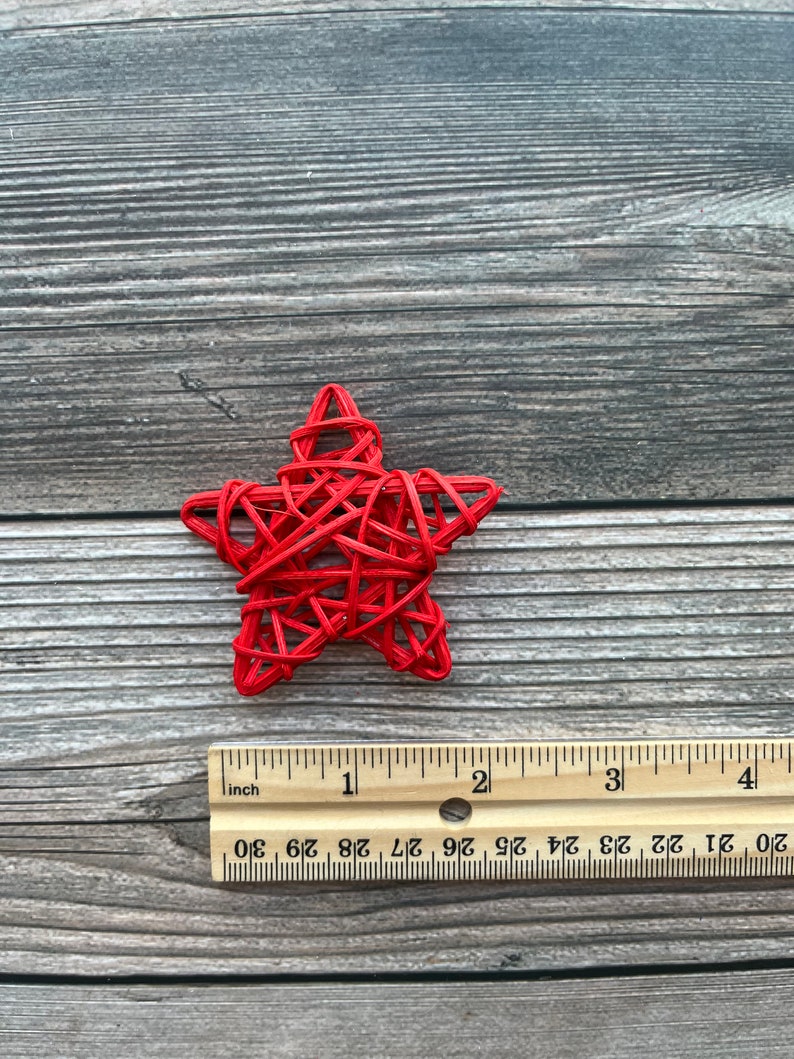 May include: A red woven star ornament, approximately 2 inches in diameter, on a woodgrain background.