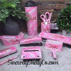 May include: A desk accessory set featuring a pink, white, and silver glitter marble pattern with the name Tristan printed on each item. The set includes a tumbler, pen, tape dispenser, stapler, scissors, pencil cup, hole punch, and note holder.