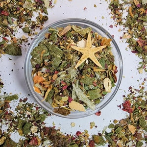 Puede incluir: Un bol de vidrio lleno de una variedad de hierbas, frutas y verduras secas. Una estrella de mar se sienta encima de la mezcla. El bol est&aacute; rodeado de una dispersi&oacute;n de los mismos ingredientes.