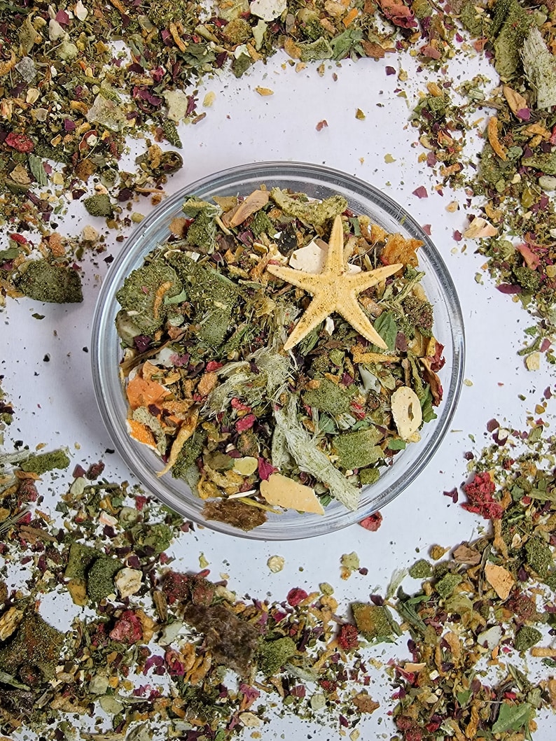 Puede incluir: Un bol de vidrio lleno de una variedad de hierbas, frutas y verduras secas. Una estrella de mar se sienta encima de la mezcla. El bol est&aacute; rodeado de una dispersi&oacute;n de los mismos ingredientes.