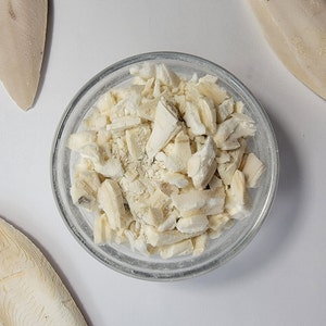 May include: A glass bowl filled with chopped, white, dried squid. There are two whole, dried squid pieces on a white surface.