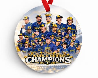 Puede incluir: Un adorno redondo de cerámica con un grupo de jugadores de béisbol con uniformes azules y amarillos. El texto dice World Series Champions 2026. Una cinta roja está unida a la parte superior. El diseño muestra un retrato de equipo.